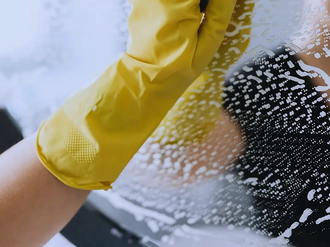 Behandschuhte Hand reinigt eine Glasfläche.